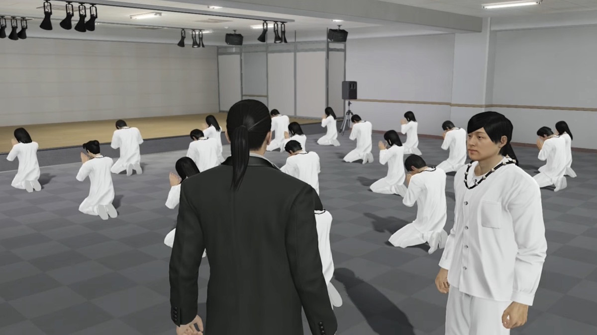 Two men stand in a large room full of people kneeling and performing odd movements.
